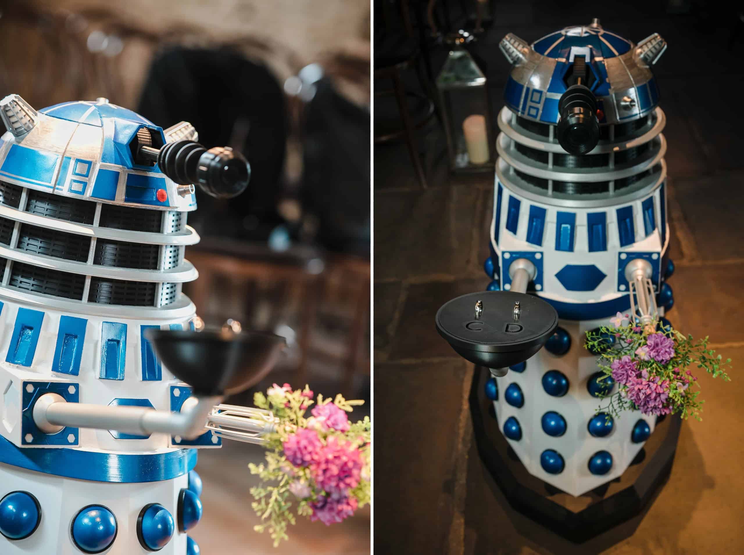 A Dalek toy positioned next to pink flowers in an outdoor garden setting. — Wedding at Cripps Barn, Cirencester