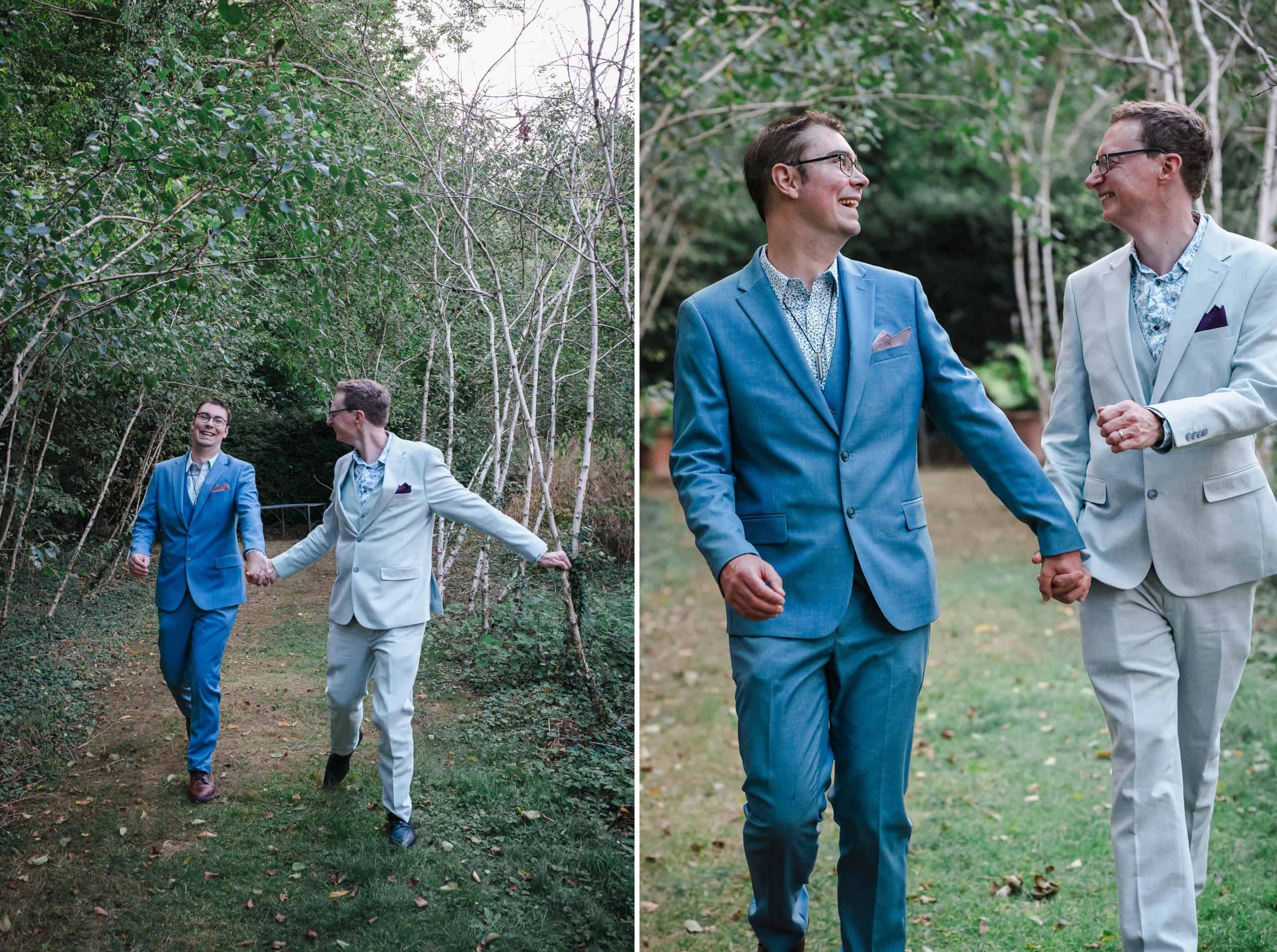 Two men in suits walking hand-in-hand down a tree-lined path, smiling at each other. — Wedding at Cripps Barn, Cirencester