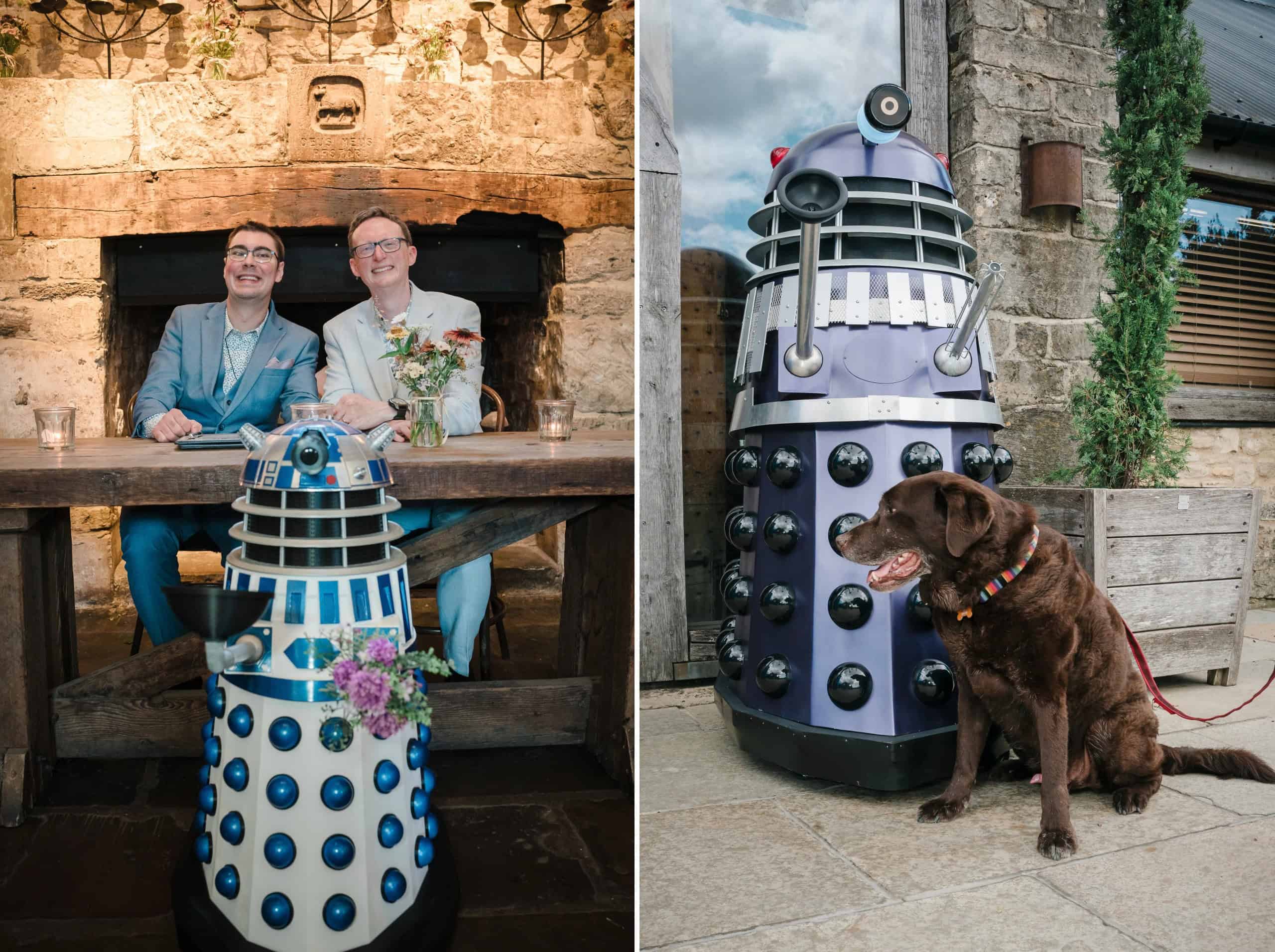 Two people seated at a wooden table with a Dalek decoration in front, smiling at the camera in a stone-walled space. — Wedding at Cripps Barn, Cirencester