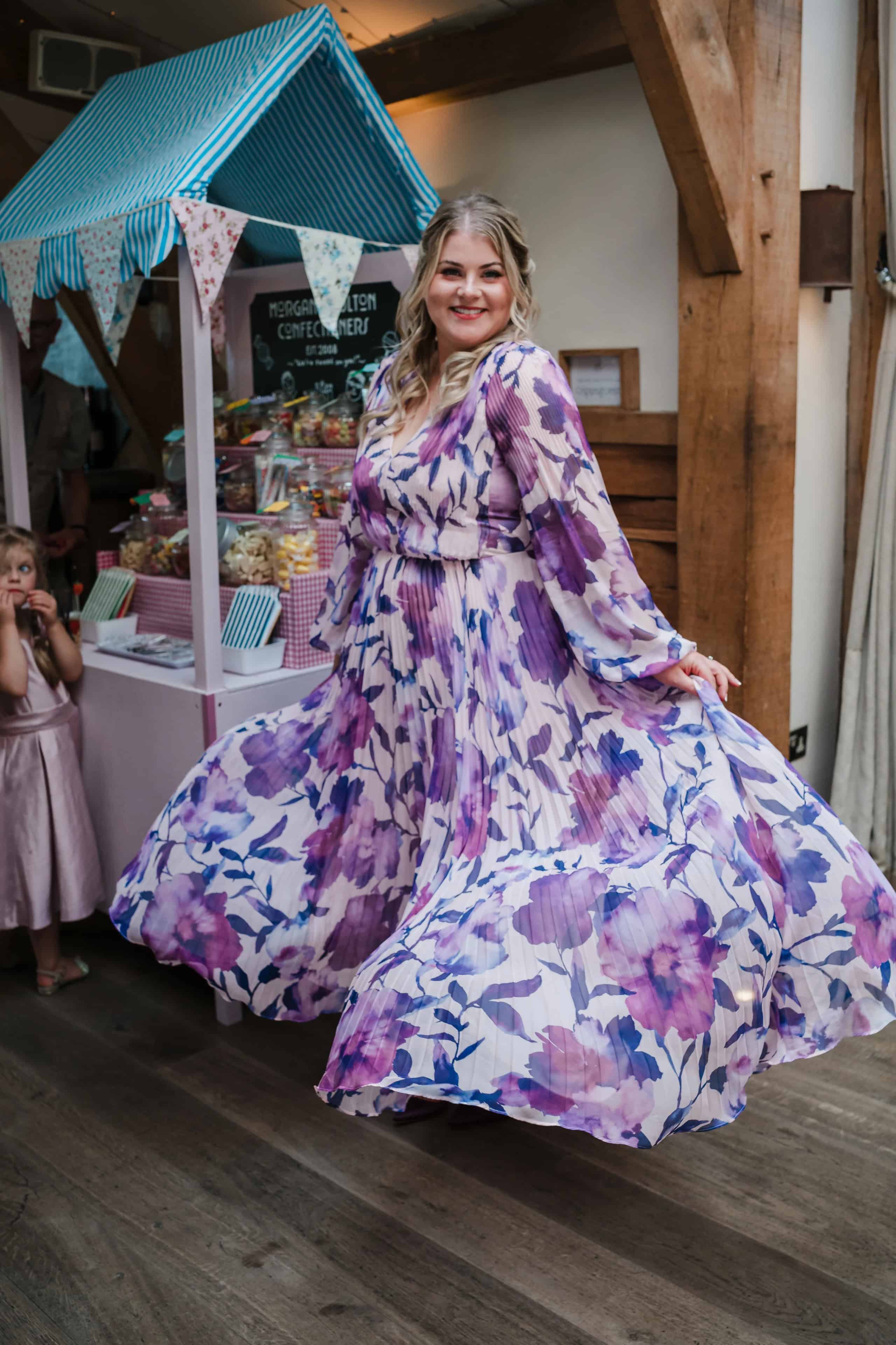 Woman in a floral dress twirls and poses in front of a decorative blue-roofed market stall display. — Wedding at Cripps Barn, Cirencester